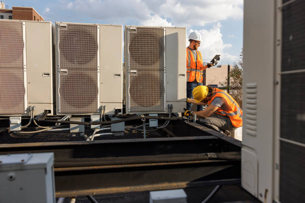 Rooftop air conditioning system inspection. Caucasian white workers check units and log the result with a portable computer.