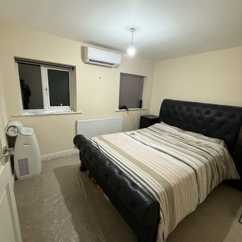 A modern bedroom wall-mounted split system installed above a bed, showing why you can leave air conditioning on overnight quietly compared to a bulky portable unit.