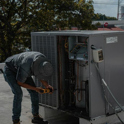 A technician from BDS Services Ltd is repairing an air conditioning unit on a rooftop, demonstrating skilled manual work.